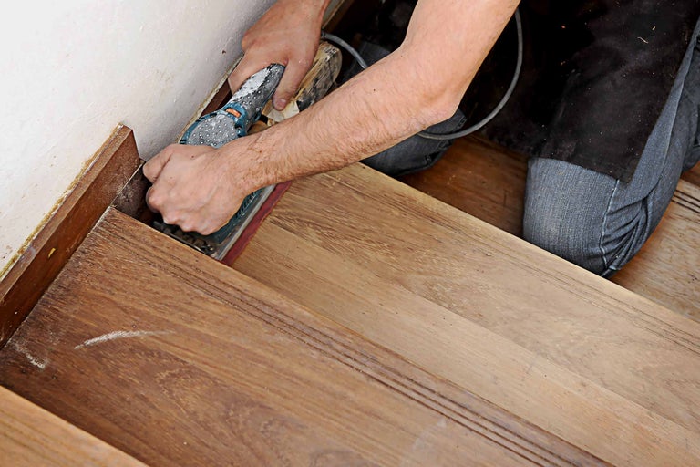 Handwerker schleift Holztreppe mit einem Schwingschleifer.