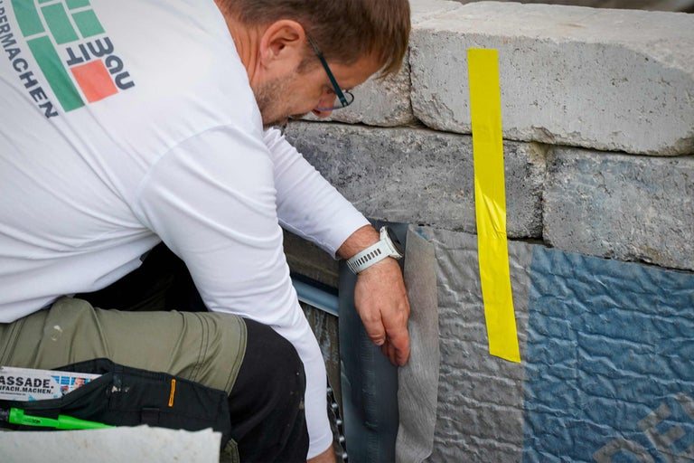 Ein Handwerker bei der Fassadeninstallation mit gelbem Klebeband und grauer Fassadenfolie.