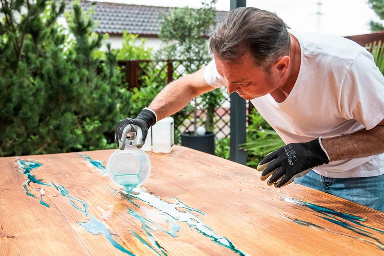 Mann gießt Epoxidharz auf Holztisch im Außenbereich
