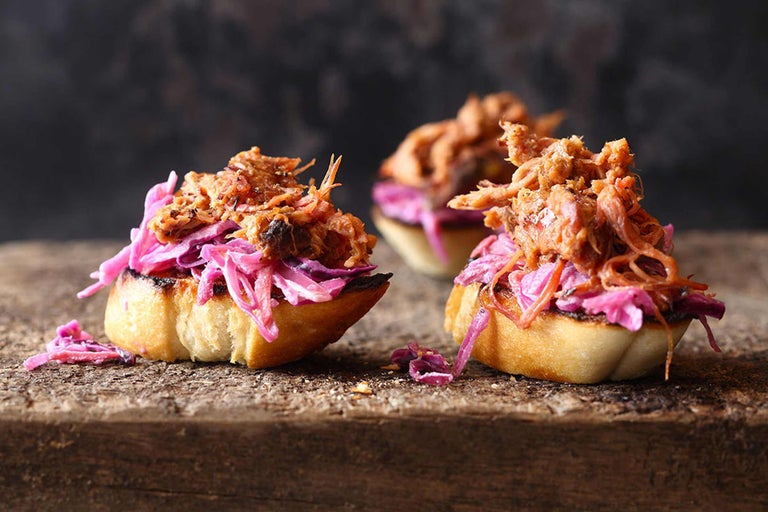 Drei Brötchen belegt mit Krautsalat und Pulled Pork auf Holzbrett