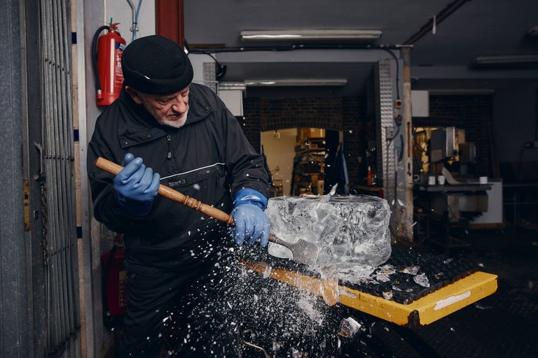 Ein Mann bearbeitet einen Eisblock mit einem Hammer und einem Meißel.