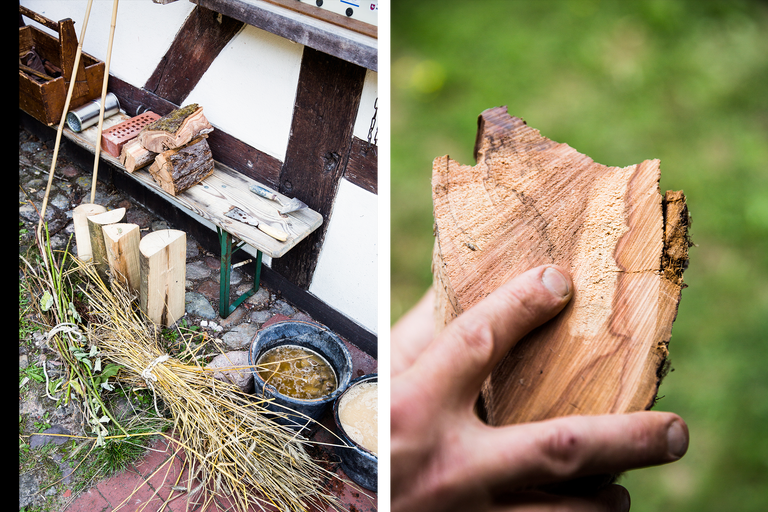 Szene mit Holz, Werkzeugen und Naturmaterialien auf einer Werkbank vor einem Fachwerkhaus.