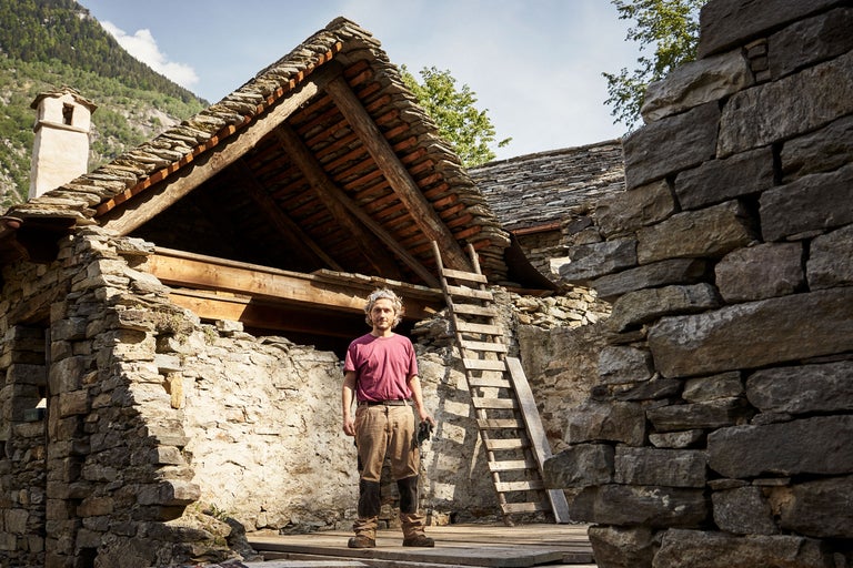 Ein Mann steht vor einem Haus mit Steindach und Steinmauern.