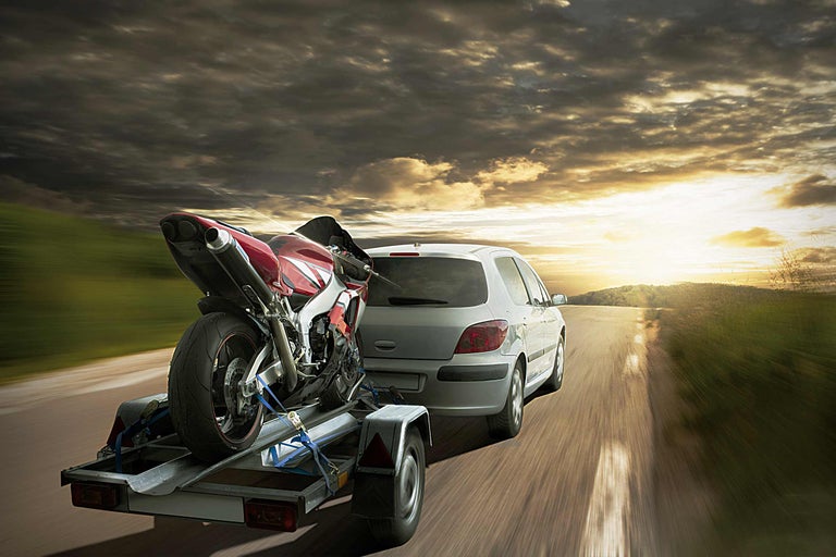 Auto mit Anhänger und Motorrad auf der Straße bei Sonnenuntergang