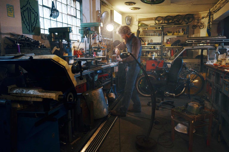 Werkstatt mit Werkzeugen, Fahrrädern und einem Mann, der an einem Projekt arbeitet.
