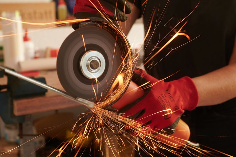 Nahaufnahme einer Person, die mit einem Winkelschleifer Metall schleift, wobei Funken fliegen
