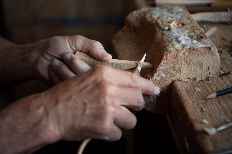 Nahaufnahme einer Person, die mit einem Schnitzmesser ein Stück Holz bearbeitet.