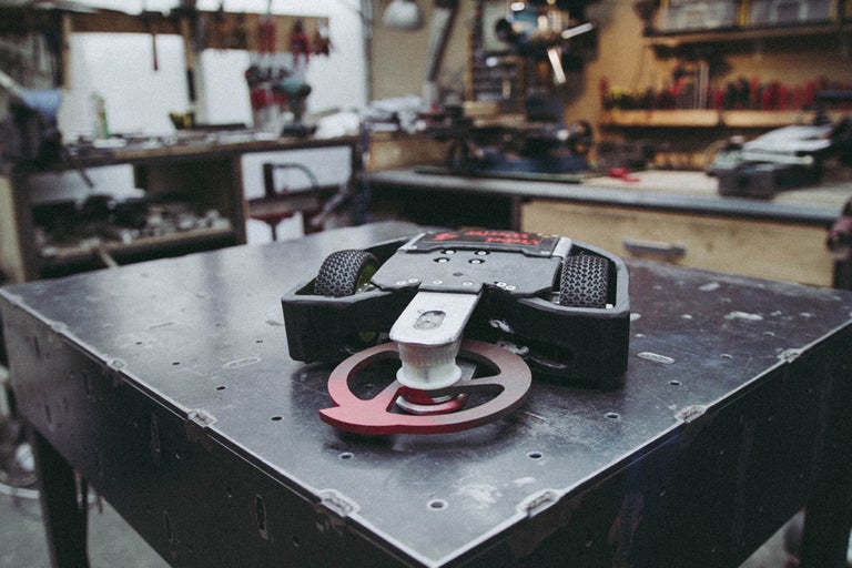 Roboter mit Rädern und einer rotierenden Waffe auf einem Tisch in einer Werkstatt.