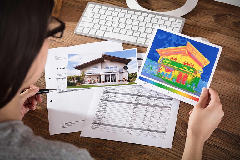 Eine Person betrachtet ein Wärmebild eines Hauses und eine Rechnung an einem Schreibtisch.