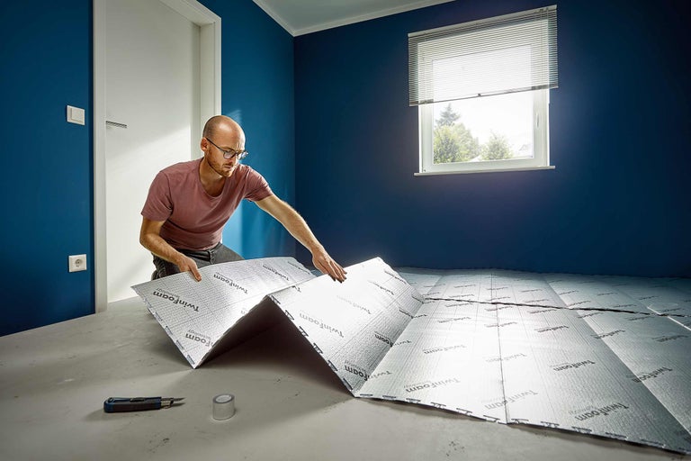 Mann verlegt Dämmunterlage Twinfoam auf einem Fußboden zur Vorbereitung für einen neuen Bodenbelag