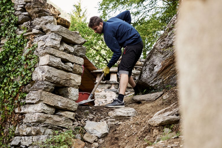 Ein Mann arbeitet mit einem Spaten an einer Trockenmauer in einem Garten.