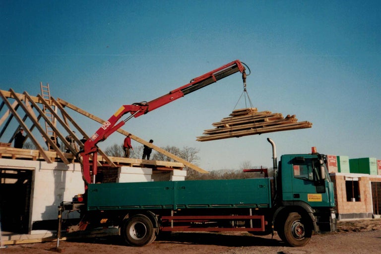Ein Kran hebt Holzlatten auf eine Baustelle für den Hausbau.