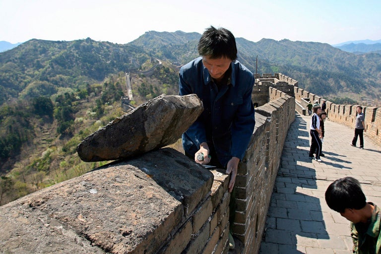 Mann repariert die Chinesische Mauer mit Stein und Werkzeug.