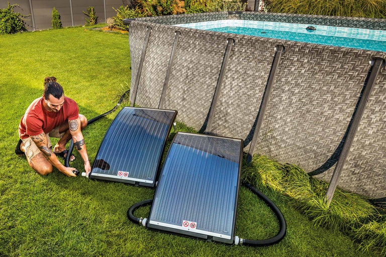 Ein Mann installiert Solarabsorber neben einem Gartenpool zur Poolheizung.