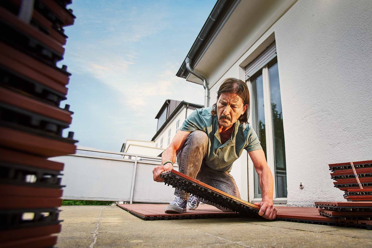 Mann verlegt Klickfliesen auf einem Balkon
