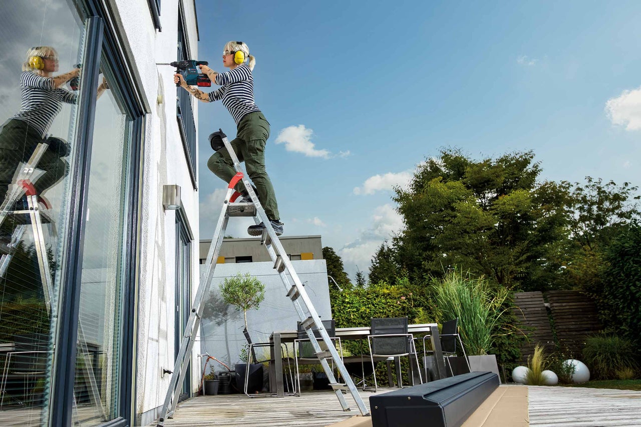 Ein Mann montiert eine Markise an einer Hauswand über einer Terrassentür.