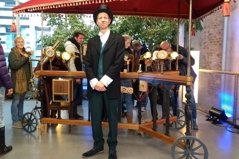 Mann im Anzug mit Zylinder steht vor einem Wagen mit Teleskopen.