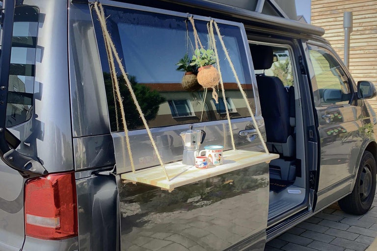 Campingvan mit an der Heckklappe befestigtem Hängetisch mit Getränken und Pflanze