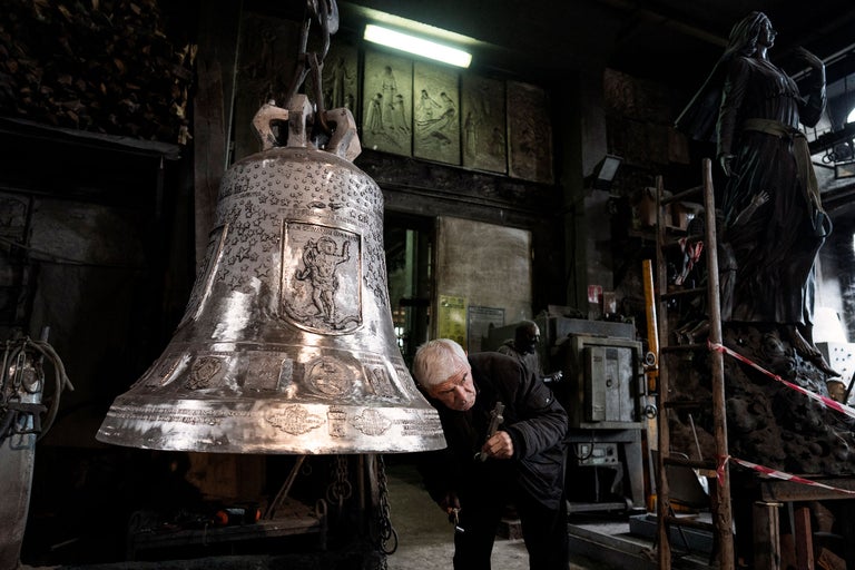 Mann überprüft große Glocke in Werkstatt mit Werkzeugen und Statuen