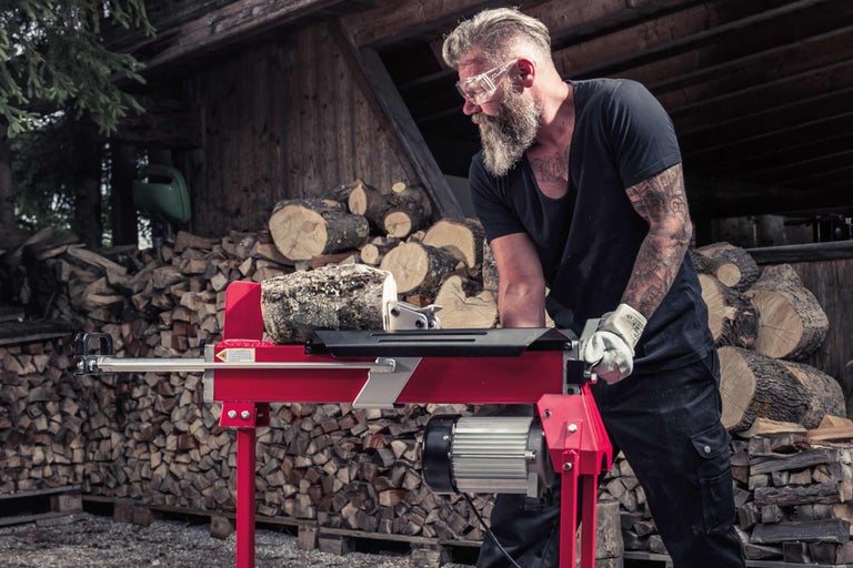 Mann spaltet Holz mit einem Holzspalter vor einem Holzstapel
