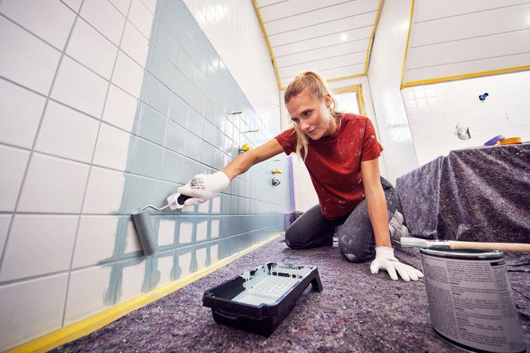 Eine Person streicht Fliesen mit einer Farbwalze.