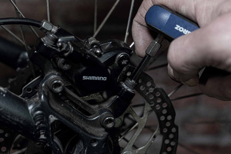 Ein Mann repariert eine Shimano Fahrradbremse mit einem Inbusschlüssel.