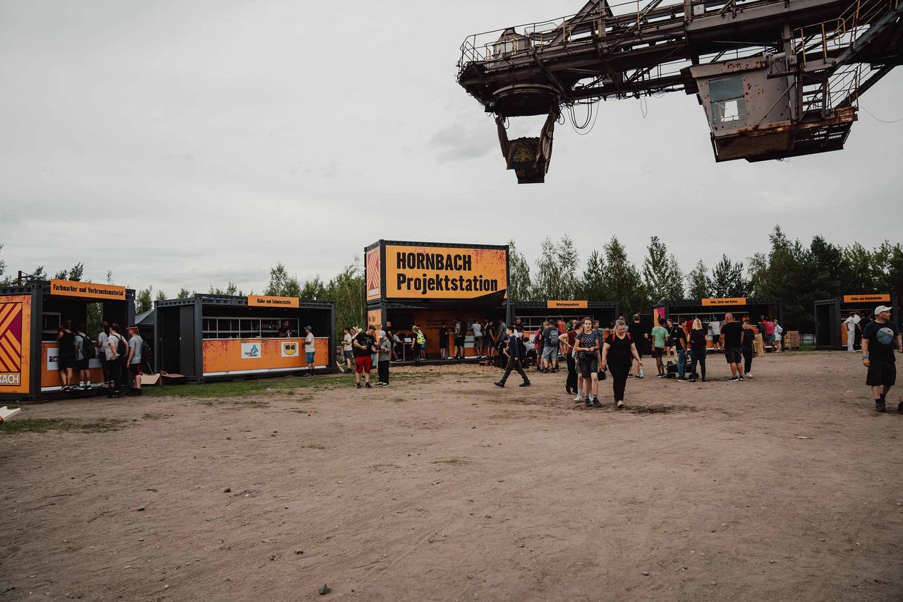 Außenansicht der Hornbach Projektstation mit Besuchern und einem Bagger im Hintergrund.