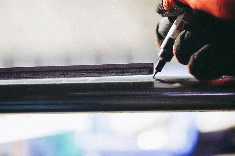 Eine Person markiert Metall mit einem Stift und einem Lineal.