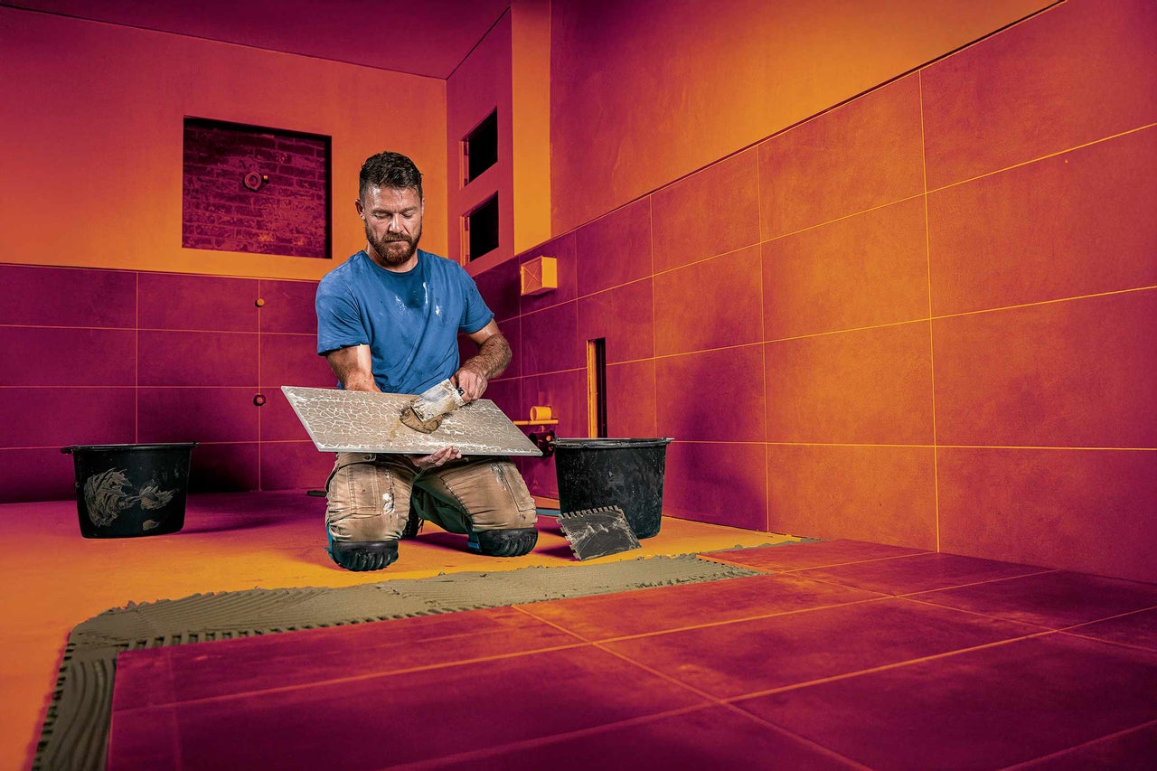 Fliesenleger bei der Arbeit im Badezimmer mit Fliesen, Eimer und Werkzeug