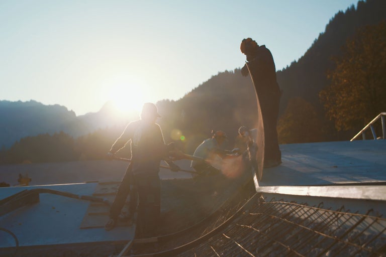 Bauarbeiter arbeiten mit Schaufeln auf einer Baustelle vor einer Bergkulisse.