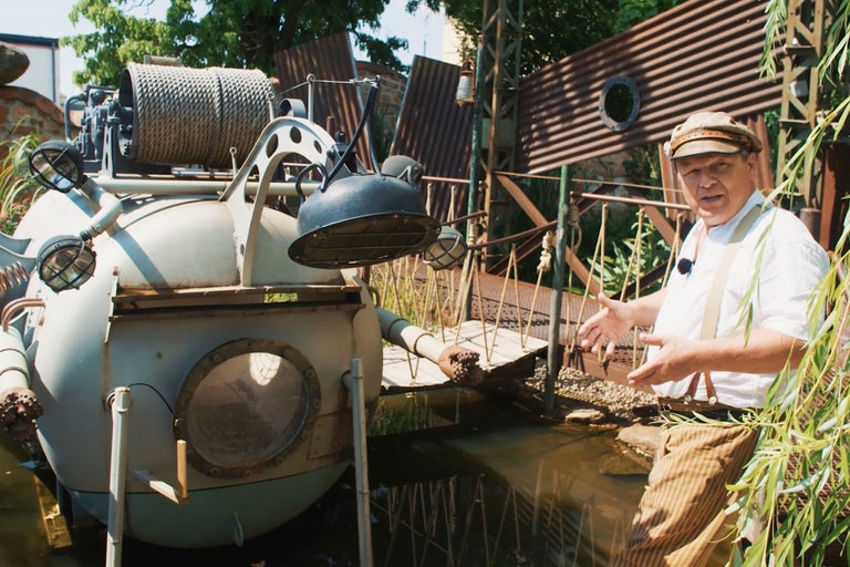 Dekorative, steampunk-artige Szene mit U-Boot-Attrappe in einem Gartenteich und einer Person.