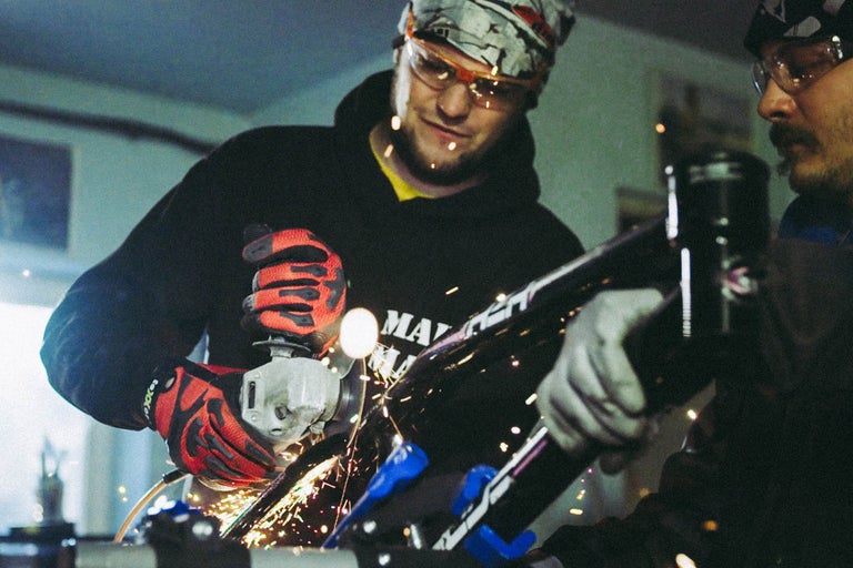 Mann arbeitet mit einem Winkelschleifer und trägt dabei Schutzbrille und Handschuhe.