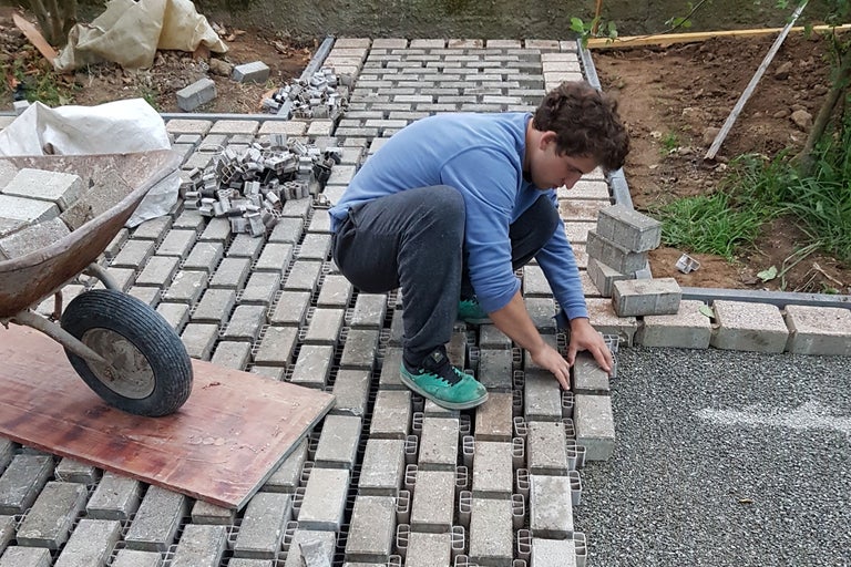 Pflasterarbeiten im Garten mit Person, Pflastersteinen und Pflasterelementen.