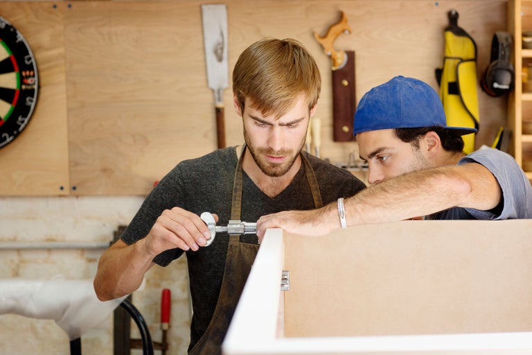 Zwei Handwerker beim Messen eines Holzrahmens mit einem Messschieber in einer Werkstatt.