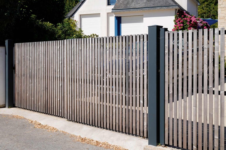 Holzzaun mit Latten und Metallpfosten vor einem Wohnhaus