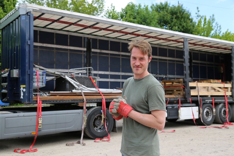 Mann mit Arbeitshandschuhen vor einem beladenen Lastwagen