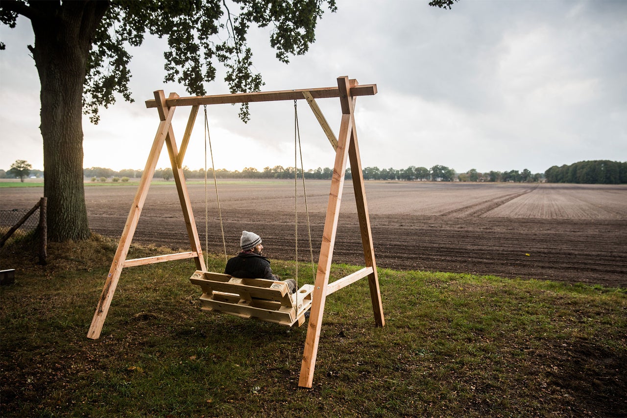 Mann sitzt auf einer Holzschaukel im Freien vor einem Feld.