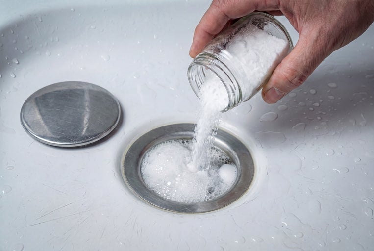 Eine Person schüttet Natron aus einem Glas in einen Abfluss.