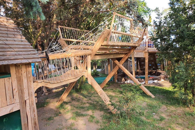 Hölzernes Spielhaus mit Hängebrücke im Garten.