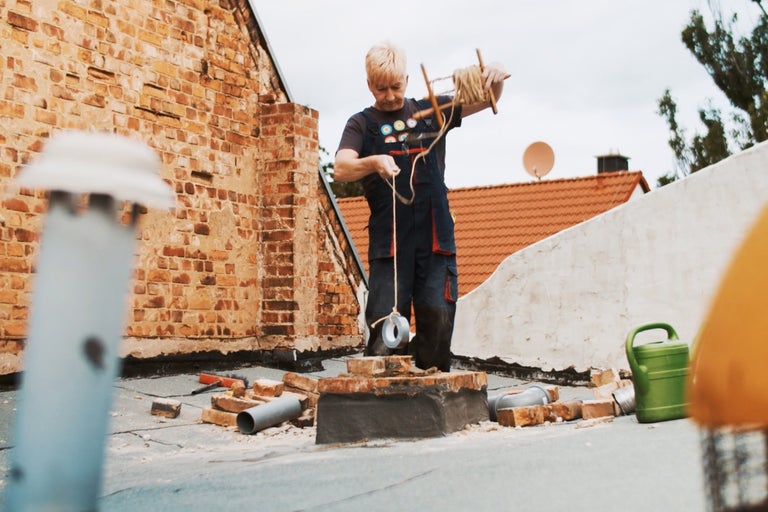 Handwerker bei Dacharbeiten mit Maurerschnur, Steinen und Werkzeugen.