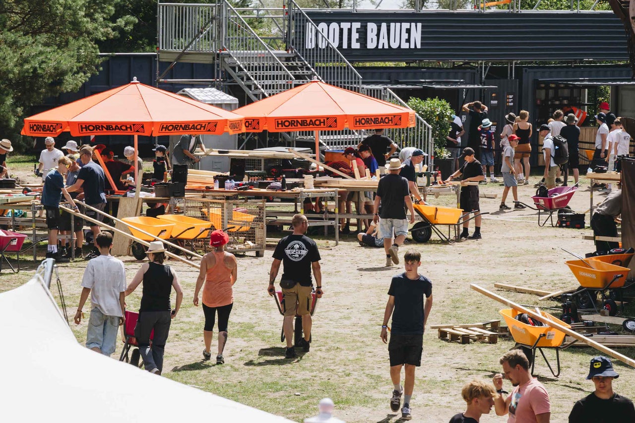 Menschen bauen an Werkbänken unter Hornbach Sonnenschirmen im Freien bei einem Event mit Material und Schubkarren.