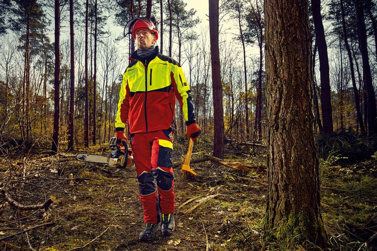 Waldarbeiter mit Schnittschutzhose, Forstjacke, Schutzhelm, Motorsäge und Sappie im Wald