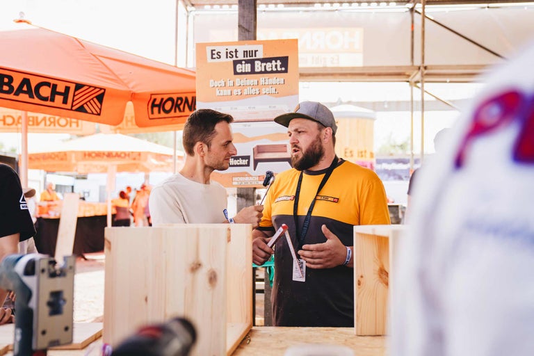 Zwei Personen im Gespräch bei einem Hornbach Event zum Thema Holzbau mit einem Informationsschild Es ist nur ein Brett