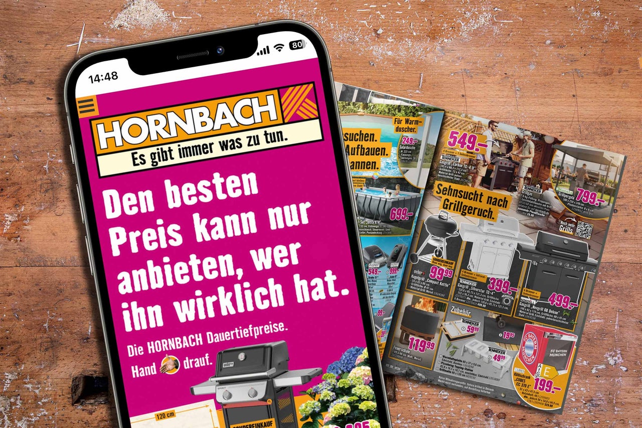 Ein Smartphone mit der Hornbach App zeigt Werbung für Dauertiefpreise auf einem Holztisch neben Prospektseiten mit Grills.