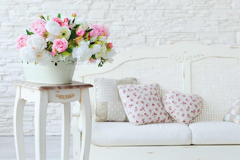 Dekorative Szene mit Blumenstrauß in einem Eimer auf einem Beistelltisch neben einem Sofa mit Kissen