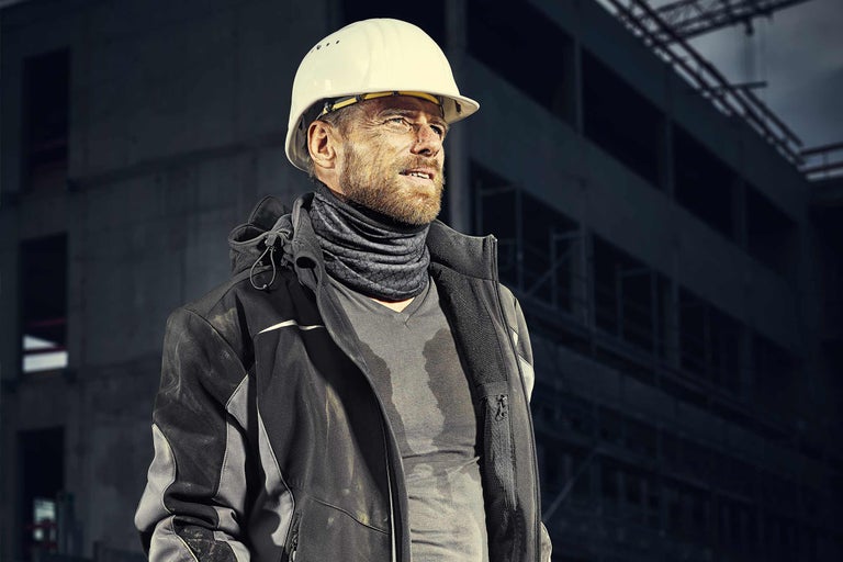 Bauarbeiter mit Schutzhelm, Arbeitsjacke und Multifunktionstuch auf einer Baustelle