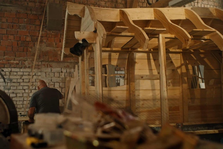 Unfertiges Holzhaus im Rohbau mit Arbeiter im Hintergrund.