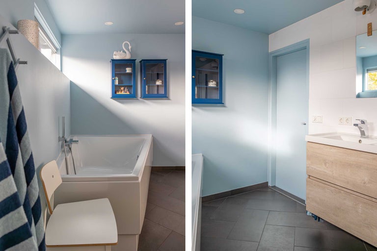 Badezimmer mit Badewanne, Waschtischunterschrank, blauen Hängeschränken und Sitzgelegenheit