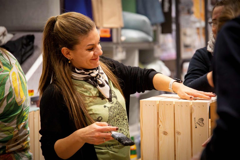 Frau streicht eine Holzkiste mit einem Pinsel.