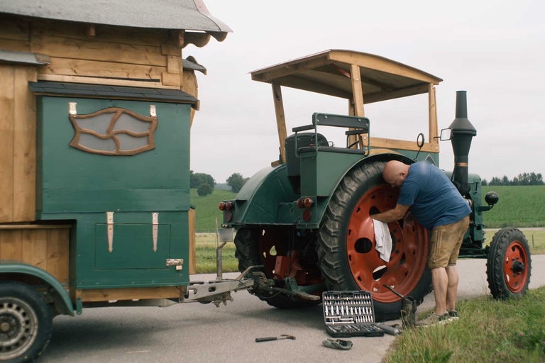 Mann wartet Oldtimer Traktor mit Anhänger auf der Straße
